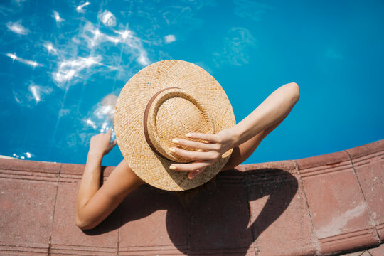 Woman wearing straw hat relaxing in pool on sunny day