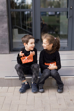 Happy siblings sitting on sidewalk and holding baskets for Halloween sweets