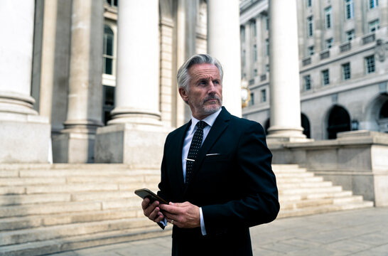 Senior businessman standing with smart phone near building