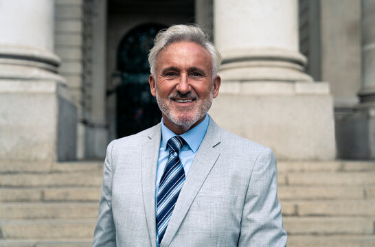 Smiling senior businessman with gray hair in front of building