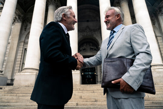 Happy senior businessman holding hands with colleague in front of building