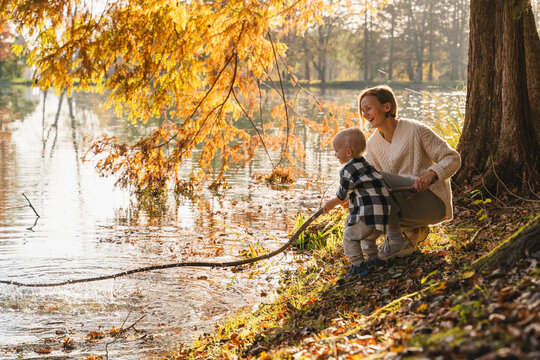 Happy mother with son holding large stick near lake in forest