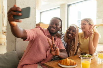 Smiling man taking selfie with friends at coffee shop
