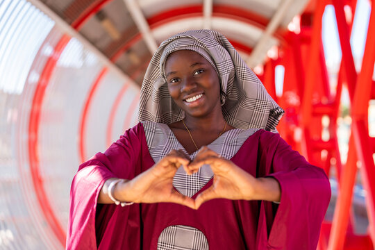 Smiling young woman with hijab gesturing heart shape on bridge