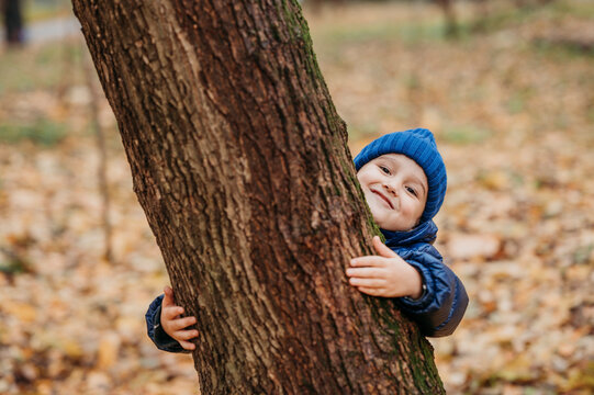 Smiling boy embracing tree at autumn park