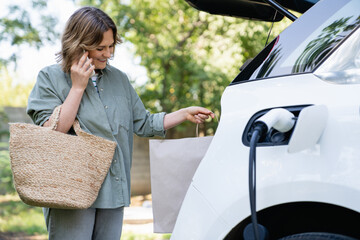 Woman with shopping bag next to a charging electric car.