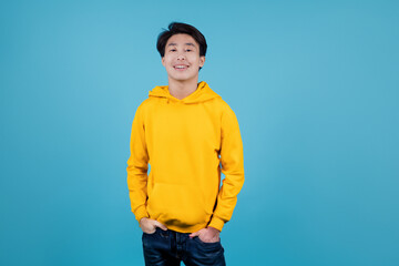 Fototapeta premium guy in a sweatshirt. a young guy in a yellow sweatshirt stands against a blue wall and smiles