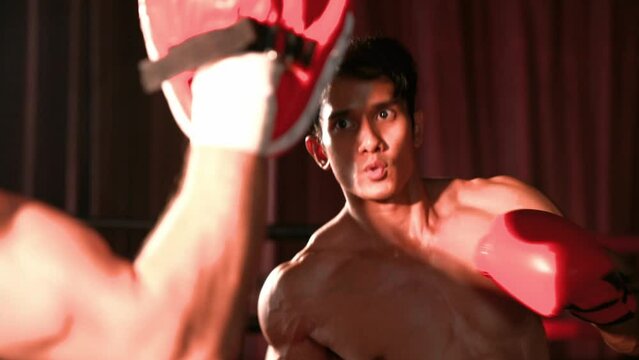 Asian and Caucasian Muay Thai boxer unleash punch in fierce boxing training session, delivering punching strike to sparring trainer, showcasing Muay Thai boxing technique and skill. Impetus