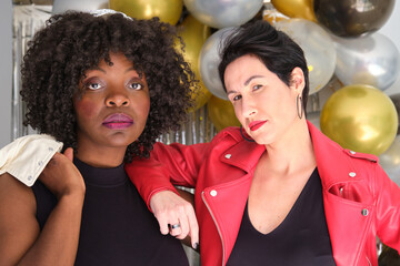 Two multiracial serious women with leather jackets in a party with balloons. - obrazy, fototapety, plakaty