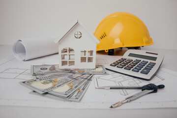 Construction drawings with helmet, calculator and model of house, cost of building
