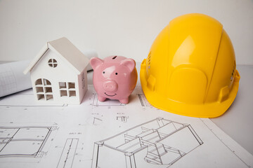 Helmet, piggy bank and model of house on blue print. Costs and savings in building
