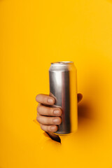 Hand holds metal jar in torn hole of yellow background. Vertical image