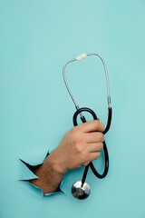 Stethoscope in a male hand on a blue background with a hole, medical concept. Vertical image
