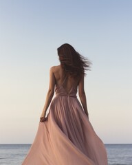 Fototapeta na wymiar A fashion-forward lady in a flowing gown stands on the beach, her dress billowing in the ocean breeze as she gazes up at the vast sky above