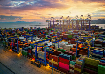 A commercial port with stacks of containers and loading cranes during sunset time - obrazy, fototapety, plakaty