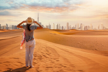 A tourist woman stands in the Red Desert and looks at the distant skyline of Dubai city, United...