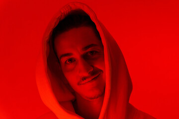 Portrait of a millennial man with glasses, red background portrait cyberstyle. Hipster in a hoodie. Selective focus