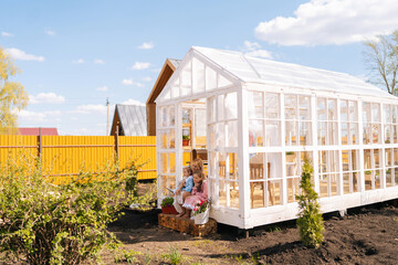 Remote view of elegance blonde young mother in dress sitting on doorstep of summer gazebo house...