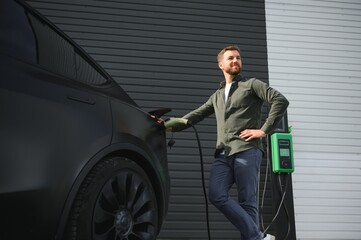 A man stands near a charging station and charges his electric car