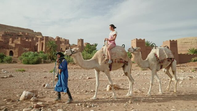 Woman riding a camel in front of Ait Benhaddou old town, Morocco