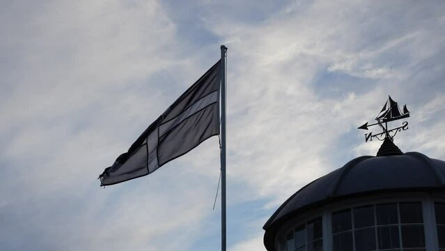 Saint Piran Cornwall flag waving in the wind, in slow motion. Kernow flag and wind vane, with cloudy sky