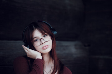 Beautiful red-haired girl in wireless headphones enjoys listening to music and one hand placed to...