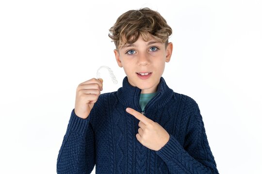 Caucasian teen boy holding an invisible aligner and pointing at it. Dental healthcare and confidence concept.