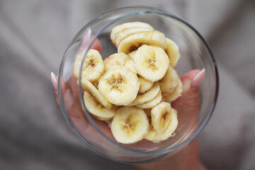 Top view banana salad. Banana slices in glass. Woman hand holding fruit slices. Transparent bowl with banana pieces.