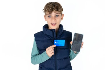 Photo of adorable  caucasian kid boy wearing blue vest  holding credit card and Smartphone. Reserved for online purchases