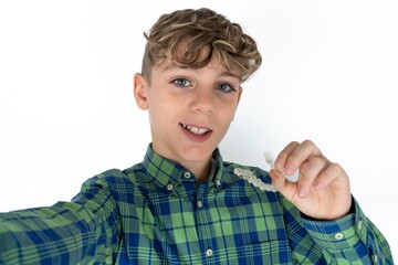 caucasian kid boy wearing plaid shirt make selfie holding an invisible braces aligner, recommending...