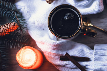 A cup of coffee on a knitted sweater, Christmas decor, garlands and a Christmas tree