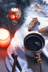 A cup of coffee on a knitted sweater, Christmas decor, garlands and a Christmas tree