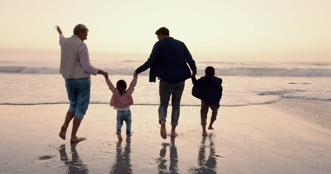 Parents, kids and holding hands with back, beach and outdoor at sunset with skipping, running and freedom. Mother, father and young children with care, bonding and walking by waves, sand and vacation