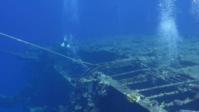 Group of scuba divers swimming on the rusty shipwreck. Remains of the ship underwater, with scuba tourist. Video from dive, seascape with wreck and people.