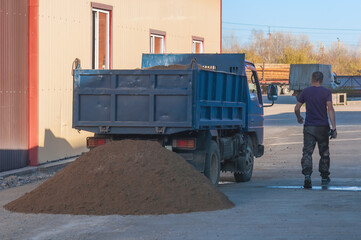 A small dump truck dumps sand from its back at a construction site. Yellow river sifted sand for...