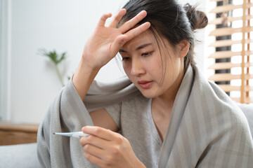 Sick day at home in winter season. Young asian woman have a fever checking thermometer and measure body temperature. © Pormezz