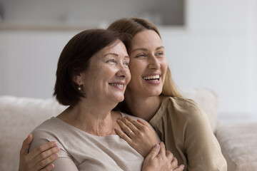 Fototapeta premium Cheerful pretty mature mom embracing, cuddling daughter on home couch, laughing, hugging adult child with love, affection, tenderness, happiness, smiling, enjoying family bonding, relation