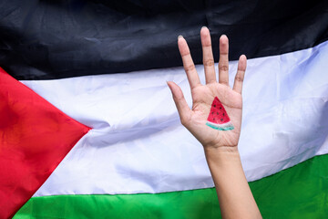Hand showing painted watermelon slice against Palestine flag background. Watermelon as a symbol of...