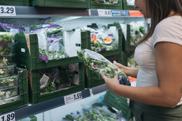 Unrecognizable young woman in the supermarket checking the properties of a bag of lettuce ready to...