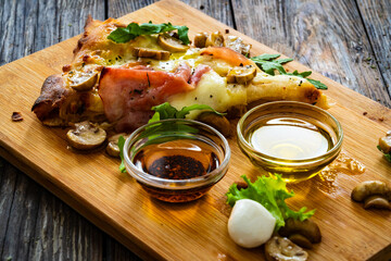 Slice of pinsa Romana with ham, mozzarella cheese and white mushrooms on wooden table

