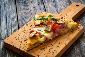 Slice of pinsa Romana with ham, mozzarella cheese and white mushrooms on wooden table

