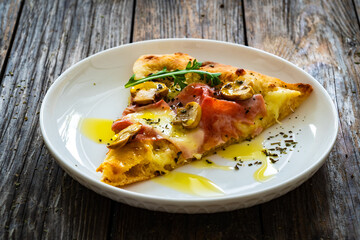 Slice of pinsa Romana with ham, mozzarella cheese and white mushrooms on wooden table
