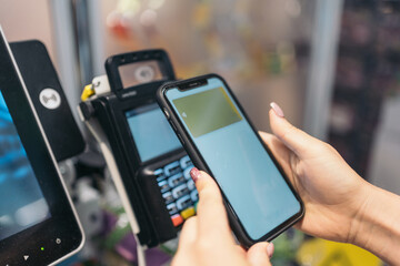 Hands of unrecognizable young woman making electronic payment with her mobile phone. Digital payment made with a smartphone at a supermarket self-service express checkout POS.