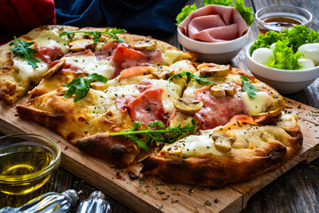 Pinsa Romana with ham, mozzarella cheese and white mushrooms on wooden table
