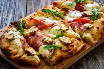 Pinsa Romana with ham, mozzarella cheese and white mushrooms on wooden table
