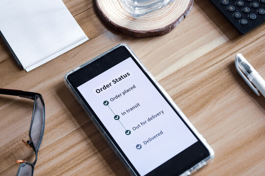 Online purchase order status on the smartphone. Wooden desk background, delivery tracking concept.