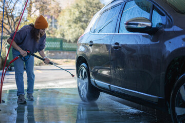 Woman cleaning auto with high pressure water jet at a self-service car wash in countryside