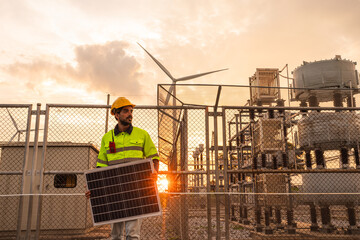 Engineer wearing uniform holding solar panels and inspection work in wind turbine farms at sunset...