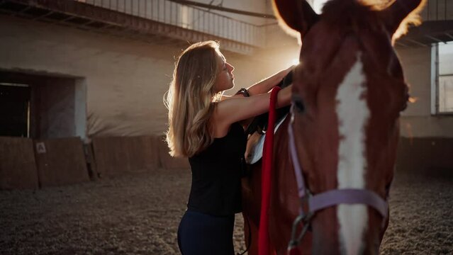 Jockey puts saddle on brown horse back on sports arena