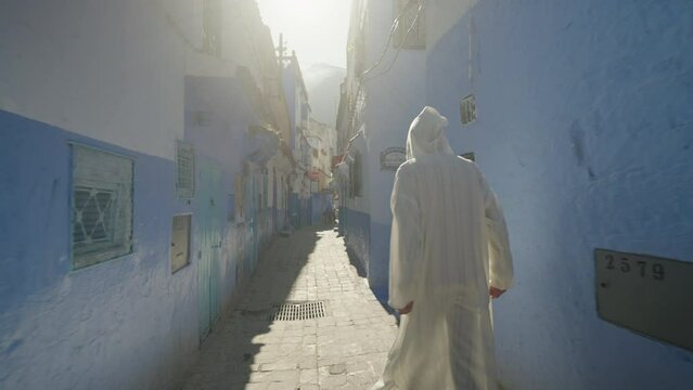 Man with traditional robe walking in the blue streets of Chefchaouen, Morocco